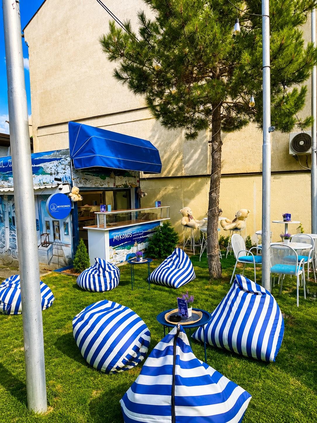Striped beanbags scattered across the grass in front of the blue-awninged Mykonos kiosk