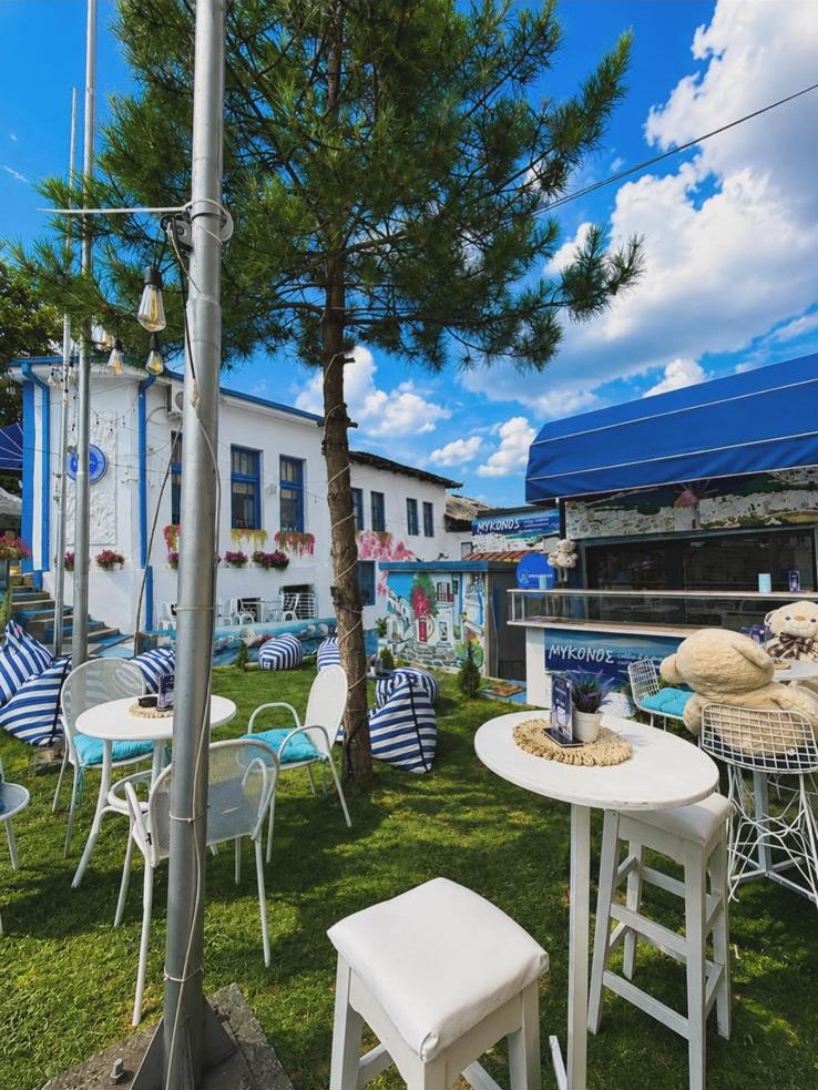 The garden in full sun: white bistro tables, striped beanbags and the painted Mykonos kiosk