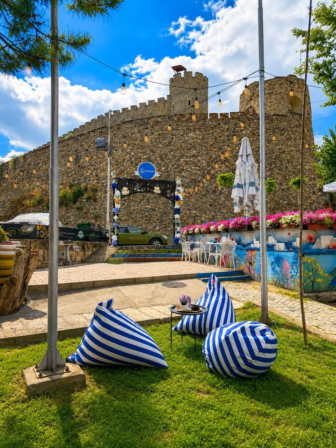 The walls and towers of Kale Fortress rising above the lawn, blue-and-white beanbags and string lights below